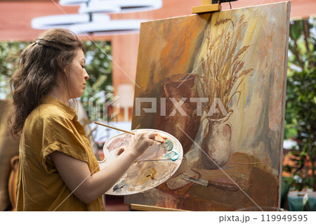 Skilled woman painting an artwork with colorful paints mixed on a palette, creating a beautiful creative paintwork with a certain painting technique in her atelier. Artist mixing watercolor. 119949595