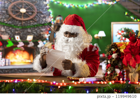 Father Christmas reading letters by the fire in his rustic log cabin, preparing presents from the North Pole workshop. Santa surrounded by festive decorations and x mas lights for seasonal cheer. Father Christmas reading letters by the fire in his rustic log cabin, preparing presents from the North Pole workshop. Santa surrounded by festive decorations and x mas lights for seasonal cheer. 119949610