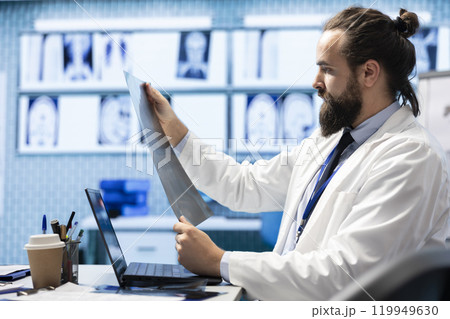 Licensed physician working on finding the right diagnostic with x ray scans results, examining bones radiography to detect illness. Medic analyzing healthcare records in hospital cabinet. 119949630