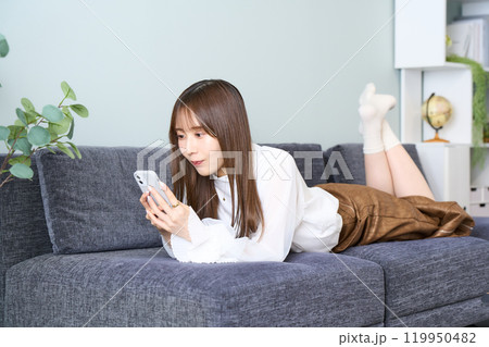 ソファーに寝そべる私服の若い女性 リビング スマホ ソファーに寝そべる私服の若い女性 リビング スマホ 119950482