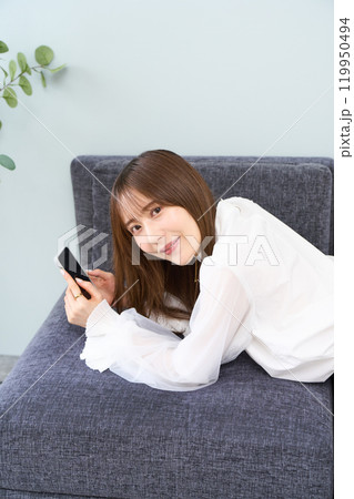 ソファーに寝そべる私服の若い女性 リビング スマホ ソファーに寝そべる私服の若い女性 リビング スマホ 119950494
