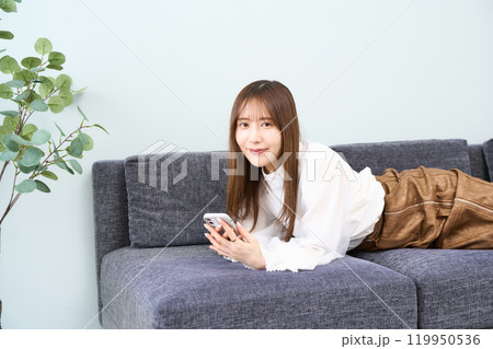 ソファーに寝そべる私服の若い女性　リビング　スマホ 119950536
