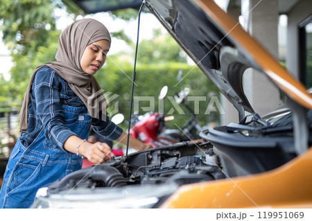 Asian muslim wear hijab woman checking up automobile engine before departure. Female trying fix their car to motor mechanic. 119951069