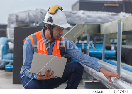 Man engineer holding laptop working at rooftop building construction. Male technician worker working checking hvac of office building. Engineering installing large air conditioning system. Man engineer holding laptop working at rooftop building construction. Male technician worker working checking hvac of office building. Engineering installing large air conditioning system. 119952421