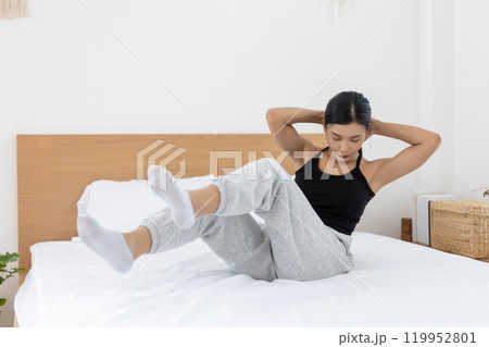 Asian young woman morning exercises after waking up on bed, Stretch feet forward. Relax and stretch and workout at home in holiday. Activity body movement arm leg. Asian young woman morning exercises after waking up on bed, Stretch feet forward. Relax and stretch and workout at home in holiday. Activity body movement arm leg. 119952801