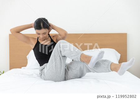 Asian young woman morning exercises after waking up on bed, Stretch feet forward. Relax and stretch and workout at home in holiday. Activity body movement arm leg. Asian young woman morning exercises after waking up on bed, Stretch feet forward. Relax and stretch and workout at home in holiday. Activity body movement arm leg. 119952802