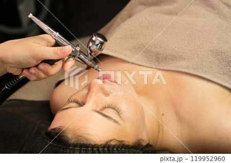 Aesthetician applying jet peeling treatment on client's face Aesthetician applying jet peeling treatment on client's face 119952960