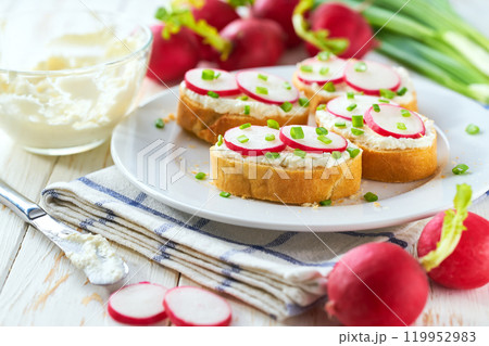 Appetizing crunchy baguette slices with cream cheese and radish slices and freshly chopped chives on a white wooden table. Appetizing crunchy baguette slices with cream cheese and radish slices and freshly chopped chives on a white wooden table. 119952983