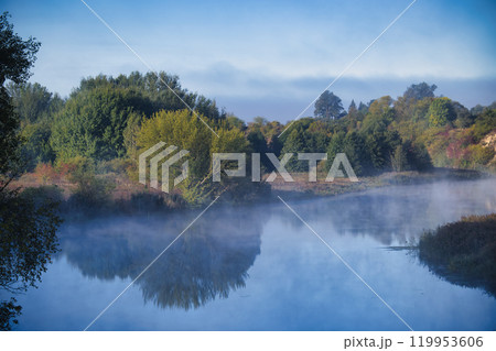Vibrant green foliage mirrored in a calm mist-covered lake evoking peace and natural beauty Vibrant green foliage mirrored in a calm mist-covered lake evoking peace and natural beauty 119953606