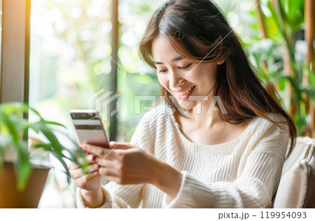 Woman smiling while using smartphone in bright room with greenery 119954093