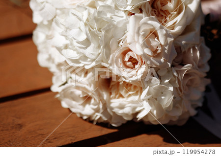 A wedding bouquet of white flowers sits on a wooden table 119954278