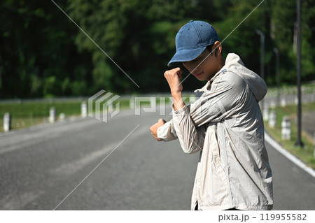 Young sportsman stretching his arms preparing for morning workout in the park 119955582