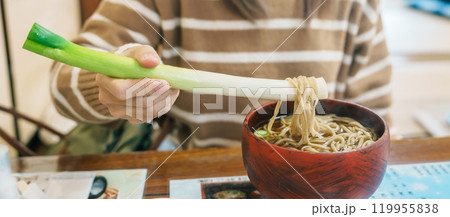 Woman tourist eating Negi Soba or Buckwheat noodles with a raw leek instead of chopsticks, famous soba when visit Ouchi Juku ancient farmer house in Shimogo, Minamiaizu, Fukushima Prefecture, Japan Woman tourist eating Negi Soba or Buckwheat noodles with a raw leek instead of chopsticks, famous soba when visit Ouchi Juku ancient farmer house in Shimogo, Minamiaizu, Fukushima Prefecture, Japan 119955838