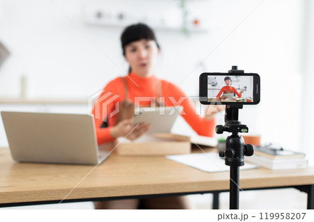 Young woman influencer unboxing tablet in online video stream Young woman influencer unboxing tablet in online video stream 119958207