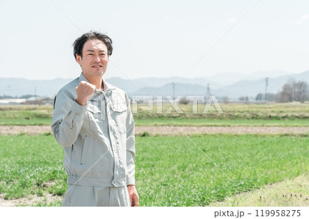 田舎の田んぼに立つ作業着姿のミドル世代の農家の男性 119958275