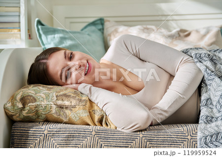 Relaxed young woman looking at camera, lying on pillow under blanket 119959524
