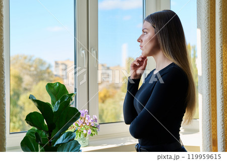 Serious young woman looking out the window Serious young woman looking out the window 119959615