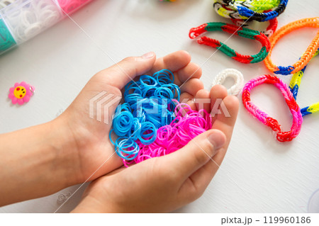 Hands holding blue and pink loom bands with other craft supplies in background. 119960186