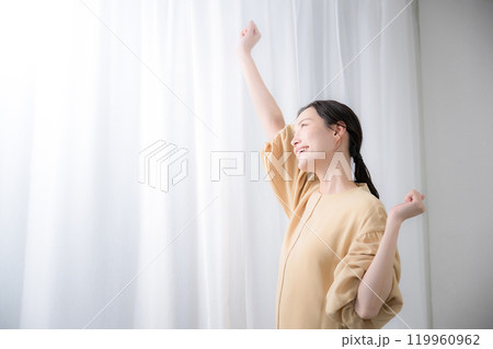 明るい日差しの差すカーテンに向かってストレッチの伸びをする女性 明るい日差しの差すカーテンに向かってストレッチの伸びをする女性 119960962