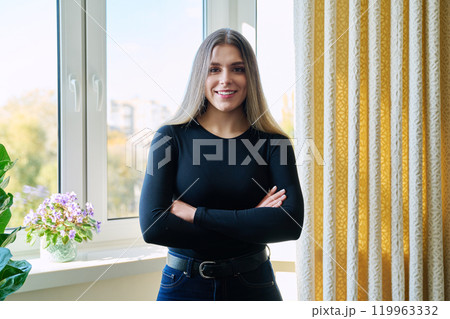 Portrait of young beautiful woman with crossed arms, at home near window Portrait of young beautiful woman with crossed arms, at home near window 119963332