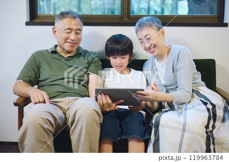 家でタブレットを一緒に楽しむ孫と祖父母 家でタブレットを一緒に楽しむ孫と祖父母 119963784