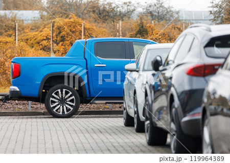 Side view of blue new ev pickup truck parked at outdoor parking lot automobile dealer or parking place against autumn foliage. Modern SUV electric vehicle outside 119964389