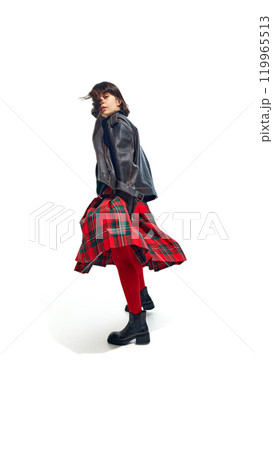 Stylish woman wearing leather jacket and red tights with plaid skirt, striking casual pose against white studio background. 119965513