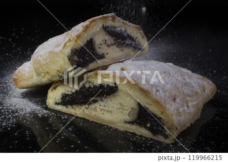 Strudel with poppy seeds sprinkled with powdered sugar cut close-up on a black background Strudel with poppy seeds sprinkled with powdered sugar cut close-up on a black background 119966215