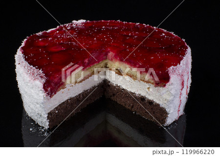 Piece of a large cake in coconut shavings with strawberries in jelly on a black background Piece of a large cake in coconut shavings with strawberries in jelly on a black background 119966220