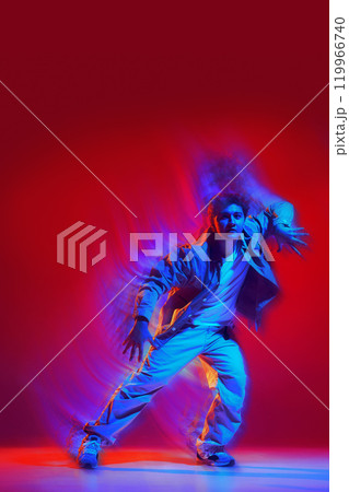 Creative design. Energetic performance of young man in casual clothes dancing hip hop, freestyle dance on red background with light wave effect Creative design. Energetic performance of young man in casual clothes dancing hip hop, freestyle dance on red background with light wave effect 119966740