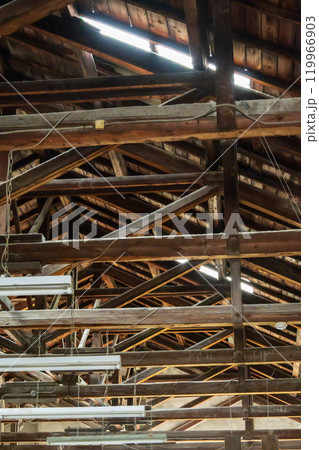 古い工場の屋根裏に組まれた柱と梁と蛍光灯 119966903