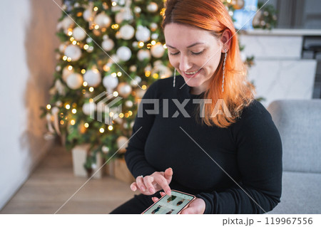 Christmas shopping. Woman shopping online holding smartphone choosing Christmas presents gifts. Girl using phone app buying new Christmas costume on Internet. Christmas winter holidays shopping sale 119967556