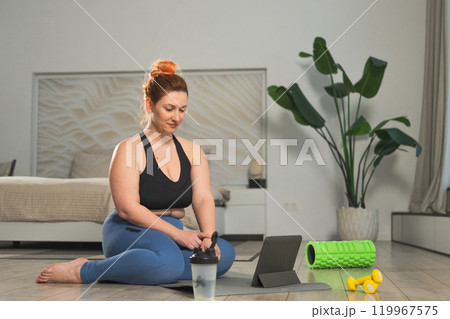 Yoga fitness workout training online. Woman practicing stretching with online app lessons at home. Plus size female doing sports exercise on yoga mat indoor. Girl have training workout for weight loss Yoga fitness workout training online. Woman practicing stretching with online app lessons at home. Plus size female doing sports exercise on yoga mat indoor. Girl have training workout for weight loss 119967575