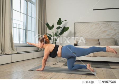 Yoga fitness workout training. Woman practicing yoga at home. Plus size female doing sports exercise on yoga mat indoor. Girl in sportswear have training workout for weight loss. Sport and fitness 119967580