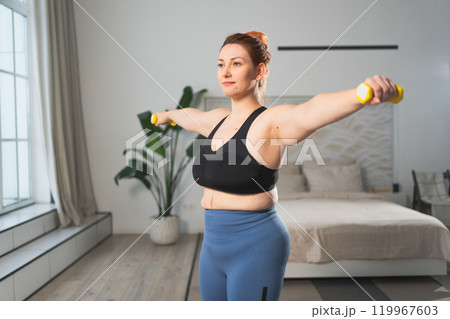 Fitness workout training. Woman picking up dumbbells. Plus size female doing sports exercise at home indoor. Girl in sportswear have workout weight training for weight loss. Sport and fitness 119967603