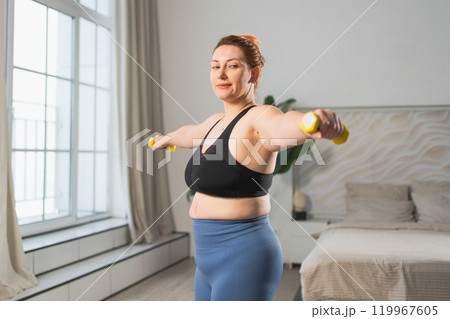 Fitness workout training. Woman picking up dumbbells. Plus size female doing sports exercise at home indoor. Girl in sportswear have workout weight training for weight loss. Sport and fitness 119967605