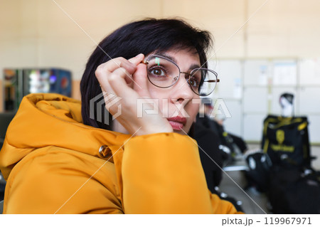 A woman with poor eyesight looks at a timetable board in a train station waiting room 119967971