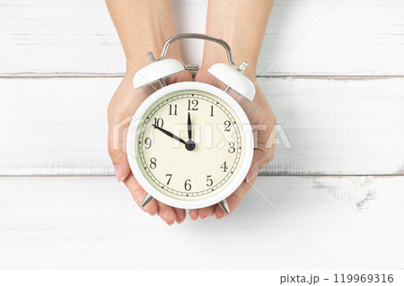 Time in Your Hands: Classic Clock Held Over White Wooden Background 119969316