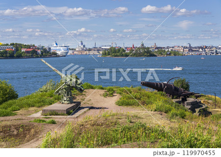 Cannons on island Lansi Mustasaari, Suomenlinna sea fortress with Helsinki city center in background, sunny summer day Cannons on island Lansi Mustasaari, Suomenlinna sea fortress with Helsinki city center in background, sunny summer day 119970455