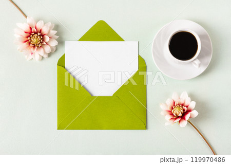 Green envelope with clean white sheet of paper for your text, black coffee and autumn flowers dahlias on green background. Invitation to the holidays. Flat lay. 119970486