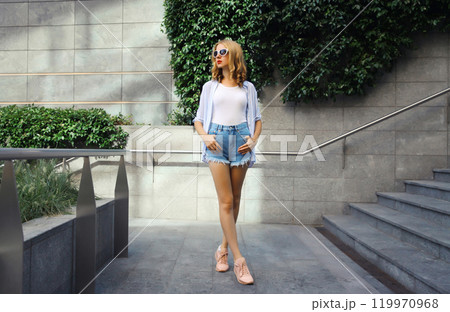 Beautiful modern young woman looking away standing on city street in summer wearing shorts, shirt 119970968