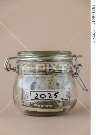 Glass jar full of American currency dollars cash banknote with text 2025 year. Preparation saving money. Moderate consumption and economy Glass jar full of American currency dollars cash banknote with text 2025 year. Preparation saving money. Moderate consumption and economy 119971265