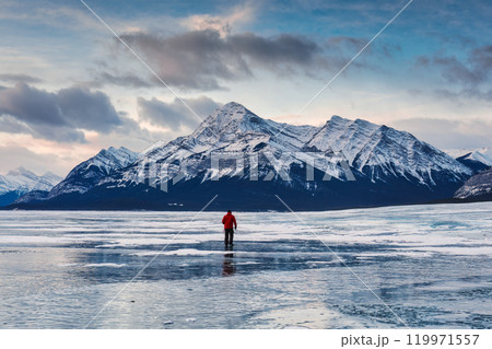 A man is walking on frozen Abraham Lake with rocky mountains in winter at Kootenay plains area, Canada 119971557