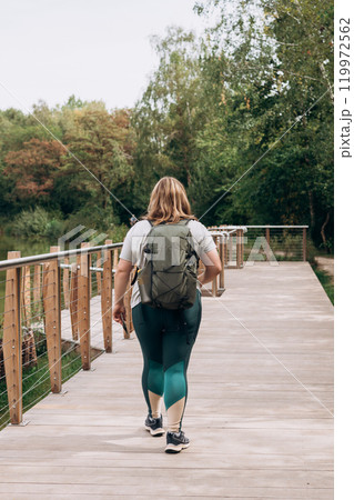 A woman hiker with a green backpack hiking near lake. Tourism and travel, Lifestyle adventure concept. 30s girl enjoying of nature. Full body, rear view A woman hiker with a green backpack hiking near lake. Tourism and travel, Lifestyle adventure concept. 30s girl enjoying of nature. Full body, rear view 119972562