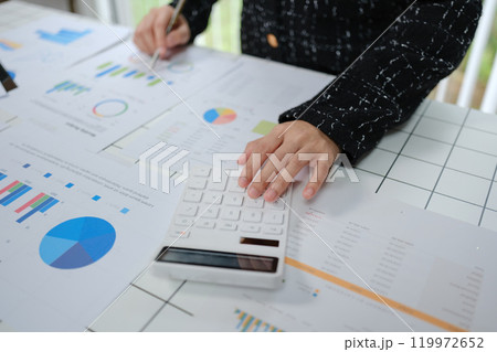 A person is sitting at a table with a calculator and a stack of papers 119972652