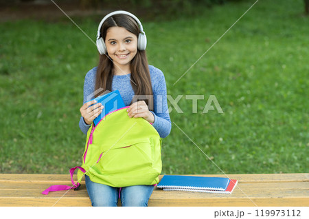 School girl listen audiobook in headphones outdoor. Back to school. Education and knowledge. Girl listening to audiobook with book. Audiobook. Student girl. School education. Student life. Copy space School girl listen audiobook in headphones outdoor. Back to school. Education and knowledge. Girl listening to audiobook with book. Audiobook. Student girl. School education. Student life. Copy space 119973112