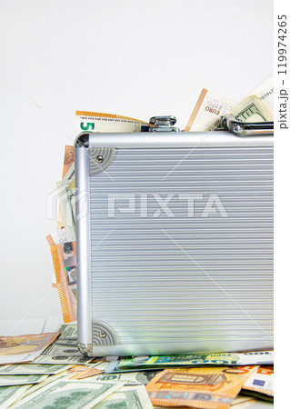 A silver aluminum suitcase overflowing with US Dollar and Euro banknotes 119974265