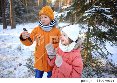 A brother and sister are joyfully engaged in a video call, set against the stunning backdrop of a snowy forest. The scene captures their laughter and connection despite the distance, with snow-covered 119976034
