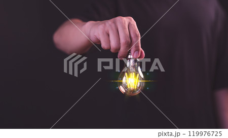 Glowing light bulb held by a male hand represents the business concepts of overcoming challenges, creative marketing, relentless problem-solving, hard work, and the pursuit of new ideas. 119976725