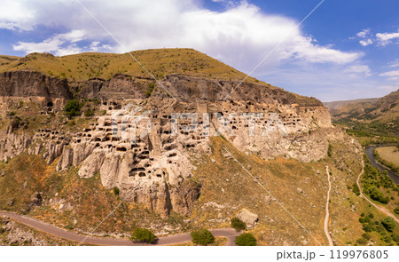 Aerial top view of Vardzia city on sunny summer day. Ancient cave monastery in Erusheti Mountain rocks at Kura River. Monument of medieval Georgian architecture, carved in rough rock. Georgia, Europe. Aerial top view of Vardzia city on sunny summer day. Ancient cave monastery in Erusheti Mountain rocks at Kura River. Monument of medieval Georgian architecture, carved in rough rock. Georgia, Europe. 119976805